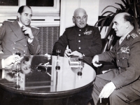 Soviet General Dmitry Danilovich Lelyushenko is centre. The latest possible date of the photograph is February 1948 when Lelyushenko visited Prague for the founding congress of the Czechoslovak-Soviet Friendship Union. Lelyushenko commanded until August 1947 the Soviet 4th Guards Mechanized Army located first in Hungary and in East Germany from May 1946, and from August 1947 he was the commander of the tank forces of the Group of Soviet Occupation Troops in Germany. Píka is a division general in the photo, so it must have been taken sometime between October 1945 and February 1948. In my opinion, the most likely date is May 1946 when Lelyushenko's army was moving from Hungary to East Germany (Soviet occupation zone) via Czechoslovakia. The man on the left is wearing a diplomatic service uniform, which would correspond to May 1946 and the working meeting of the commander of the moving Soviet troops with the Vice-Chief of the Czechoslovak Main Staff Heliodor Pika on the right. The man in the diplomatic service uniform may be a Soviet embassy guard, wearing a formal suit unlike Lelyushenko. Lelyushenko is obviously wearing a service uniform with only ribbons and no foreign decorations; he would probably not wear this on an official visit. Author of the caption: Jiří Fidler, Institute of History of the Czech Armed Forces